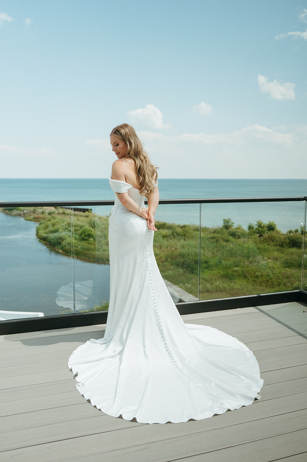 A bride in a fitted white gown on the estate balcony, Lake Huron and the shoreline behind her