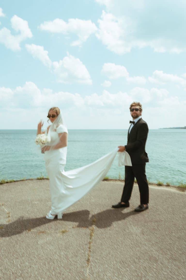 A bride and groom on the bluff above Lake Huron, her veil and train trailing across the grass