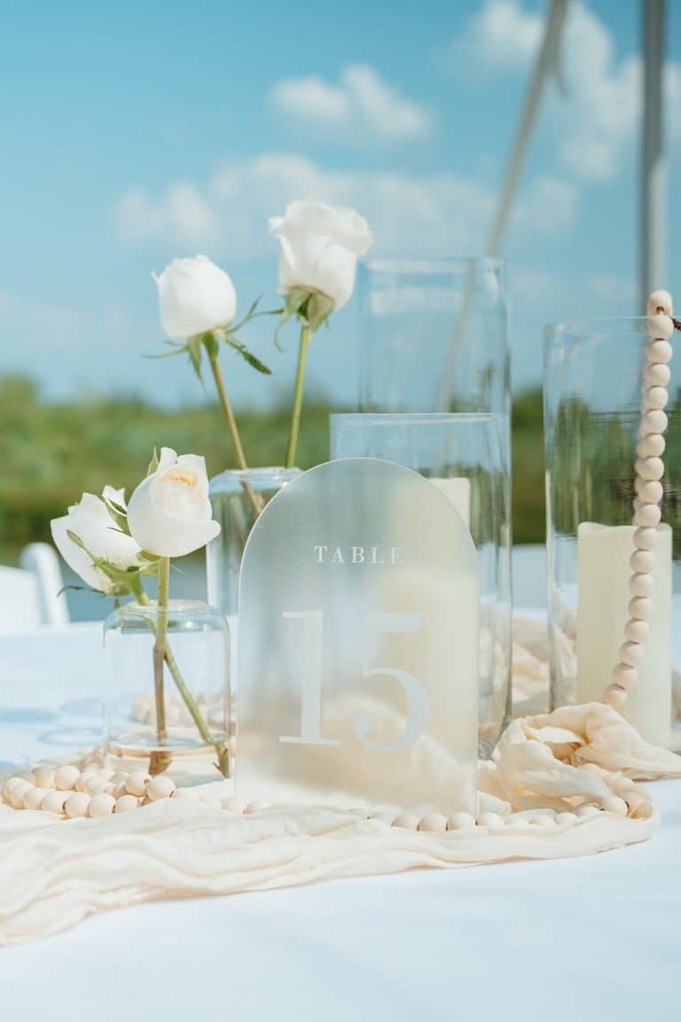 A reception table set with white roses and candles, Lake Huron glittering behind it