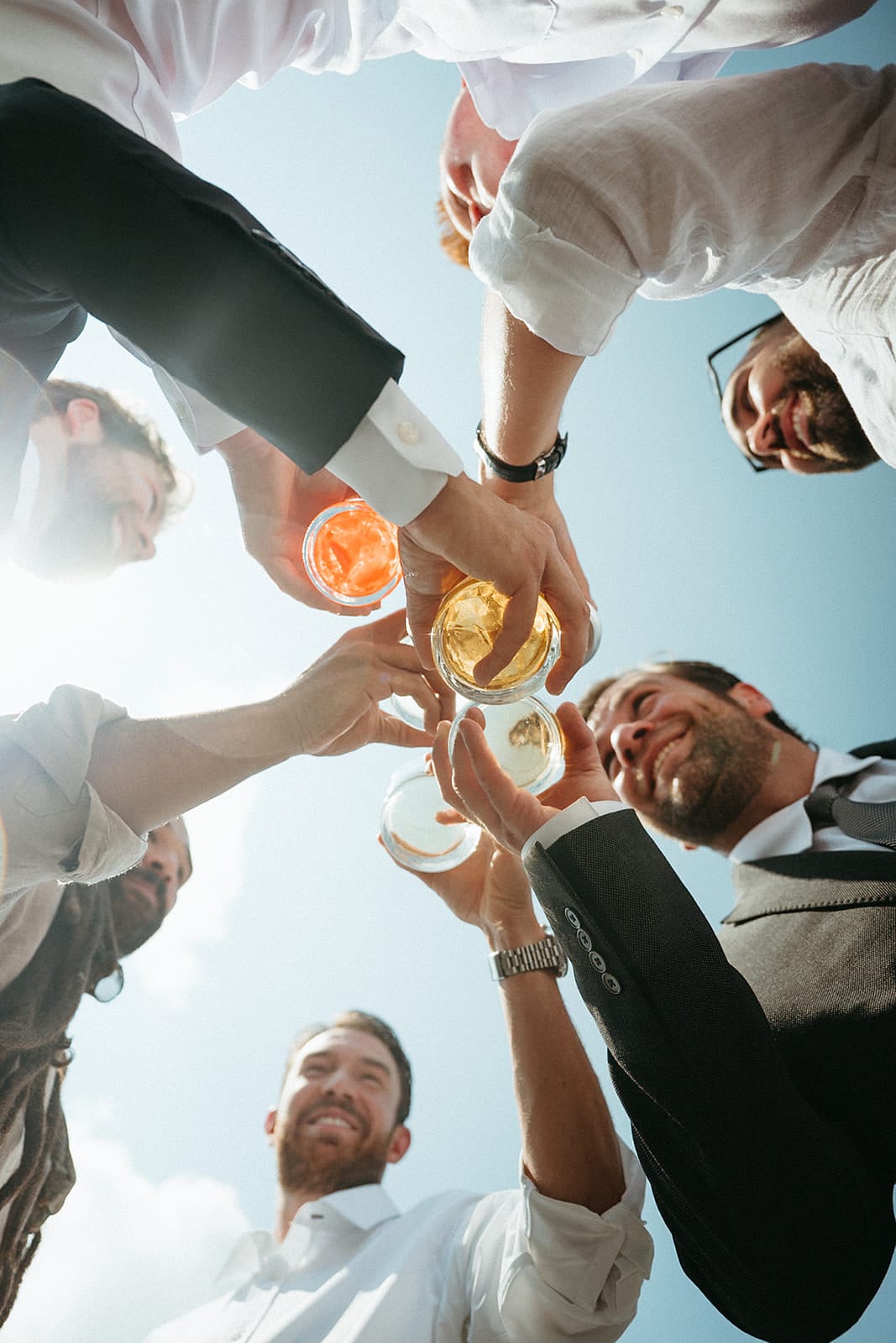 Champagne glasses raised in a toast against a bright summer sky