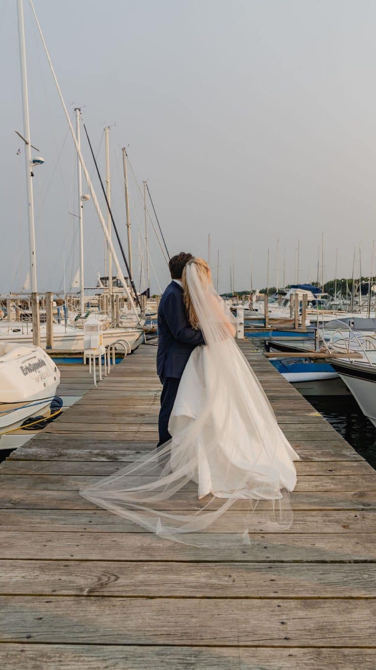 A bride and groom walking together down a dock at the harbor