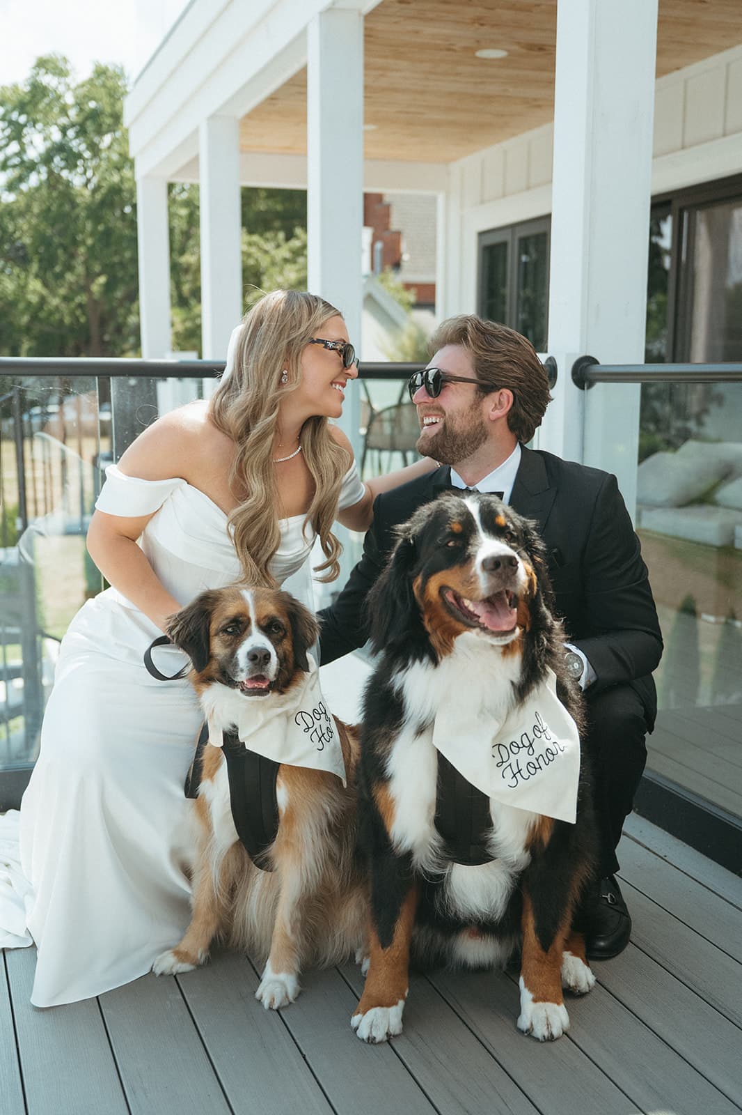 A bride and groom on the estate porch with their two dogs in matching bandanas