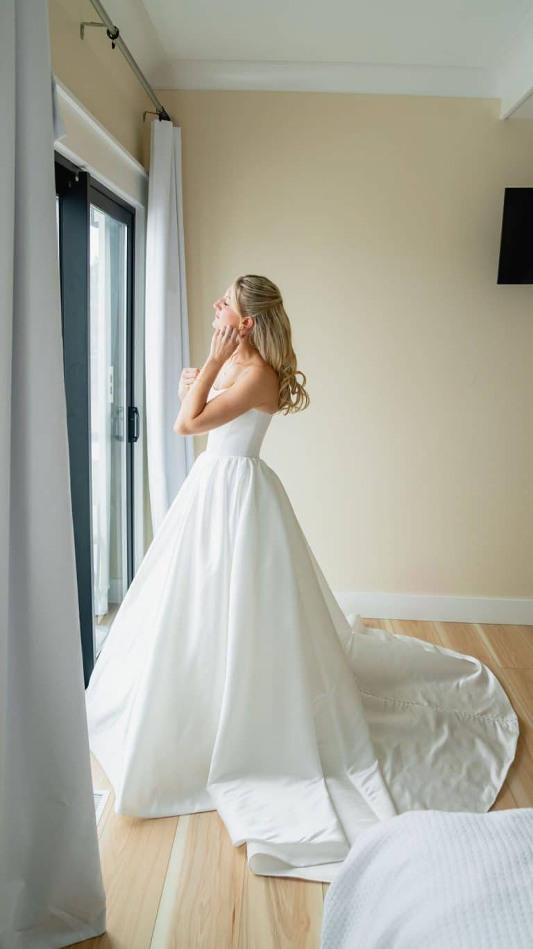 A bride in a strapless gown by a sunlit window in the estate