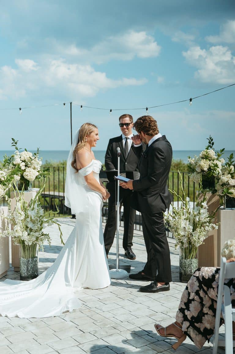 A couple exchanging vows between tall arrangements of white flowers